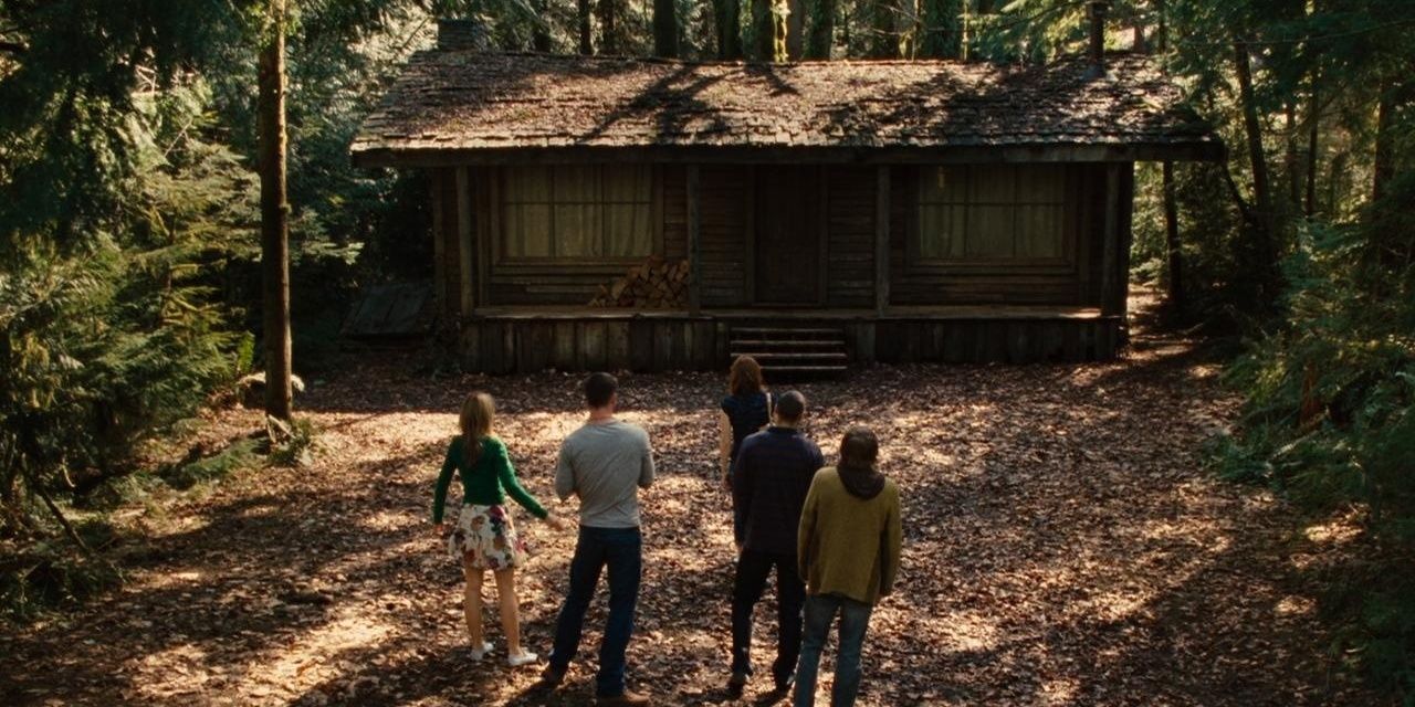 A group of people look at an old abandoned cabin in the forest.