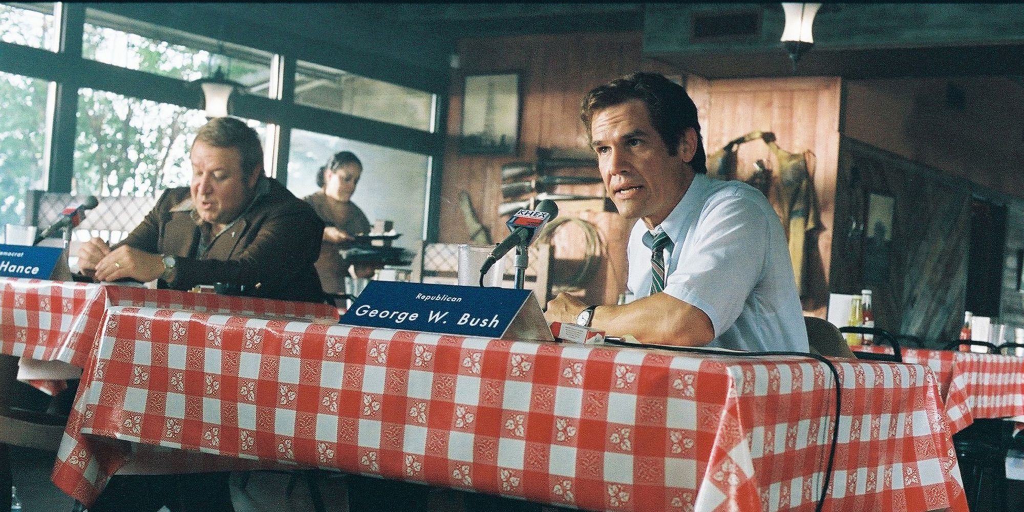 A man sits at a table and speaks into a microphone