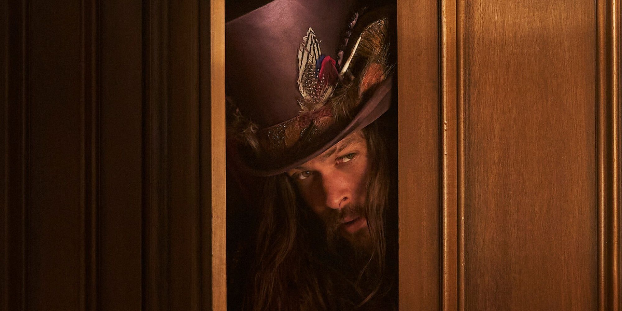 Jason Momoa as Flip, wearing a fancy top hat and peeking out from behind a door in Dreamland.
