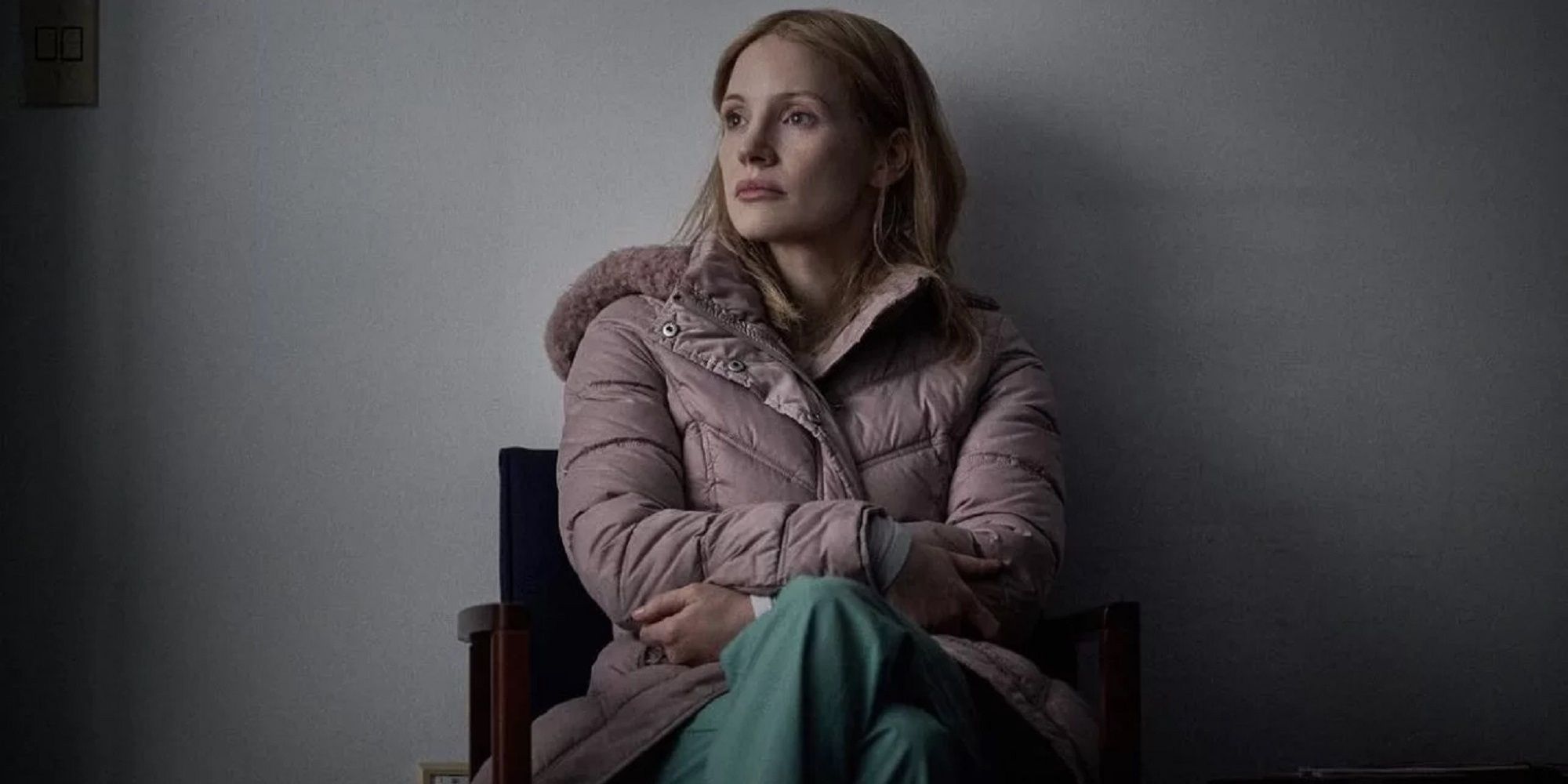 Jessica Chastain, as the nurse in The Good Nurse, sits in a chair against a blank white wall.