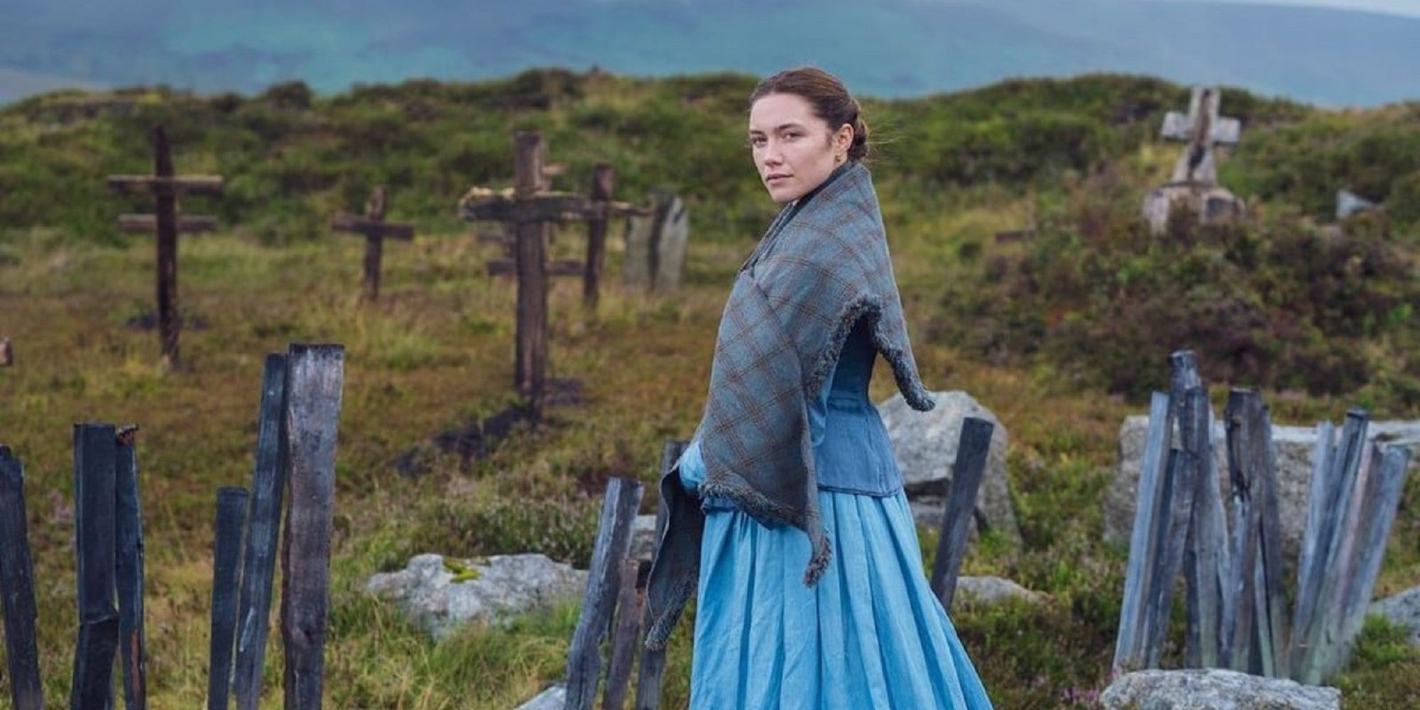 Florence Pugh as Lib, wearing a bright blue dress and standing in a graveyard in 