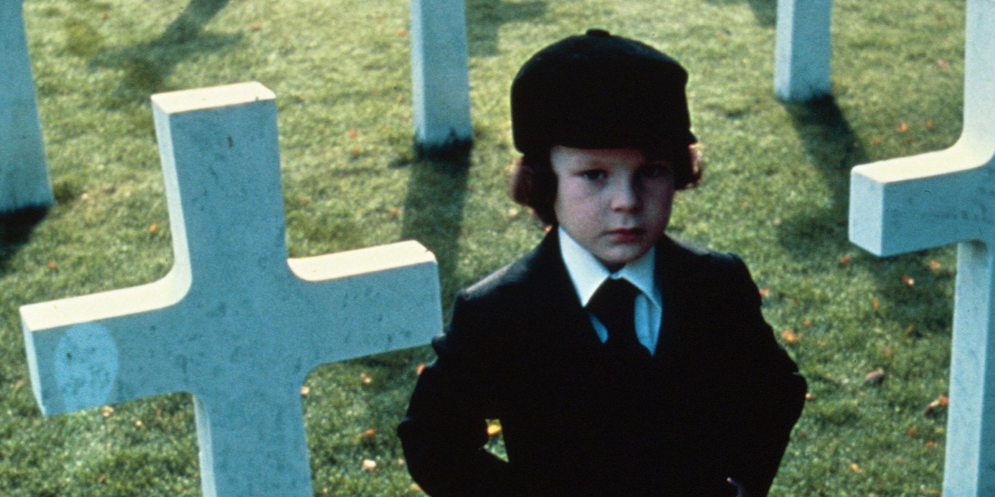 The boy stands in the cemetery next to several white crosses.