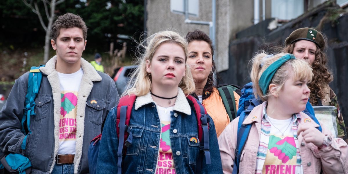 Several characters from Derry Girls stand with denim jackets and backpacks.