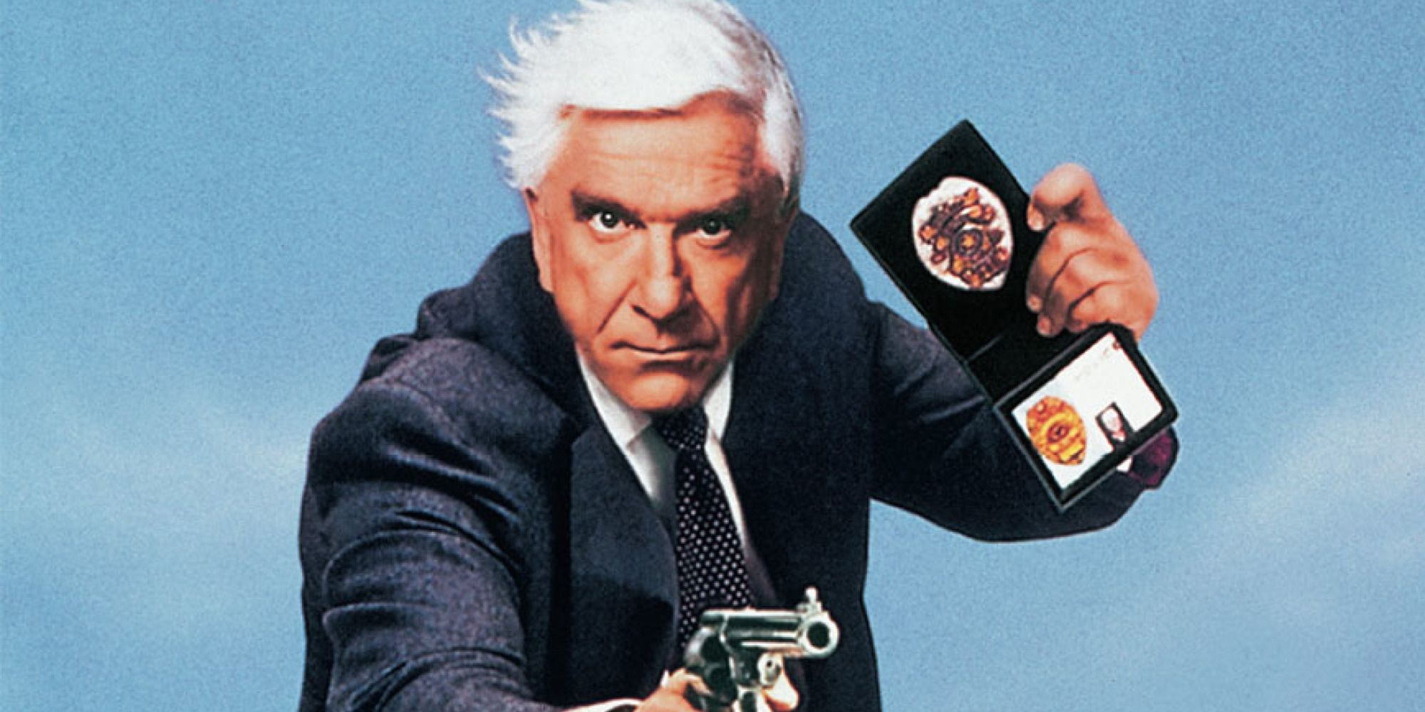 Leslie Nielsen as a suit-wearing police detective with a gun and a badge in The Naked Gun.