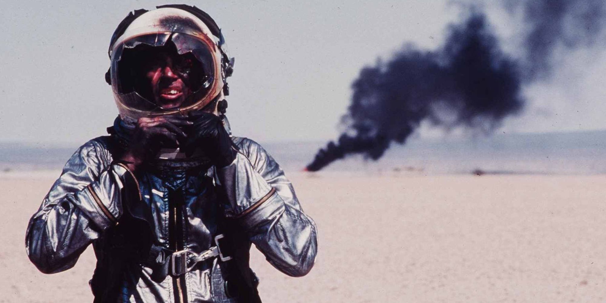 The battered astronaut is standing, and his shuttle is on fire in the background.