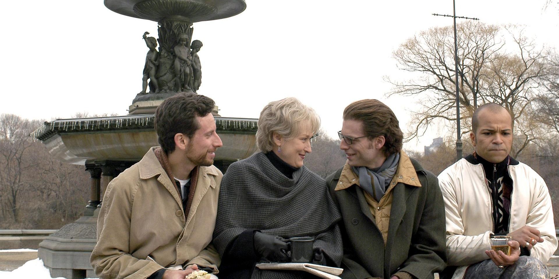 Three men are talking to a woman in front of a fountain in 