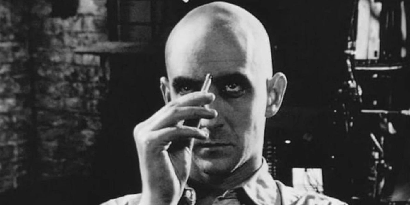 A bald man presses a pen to his forehead in the 1998 film Pi.