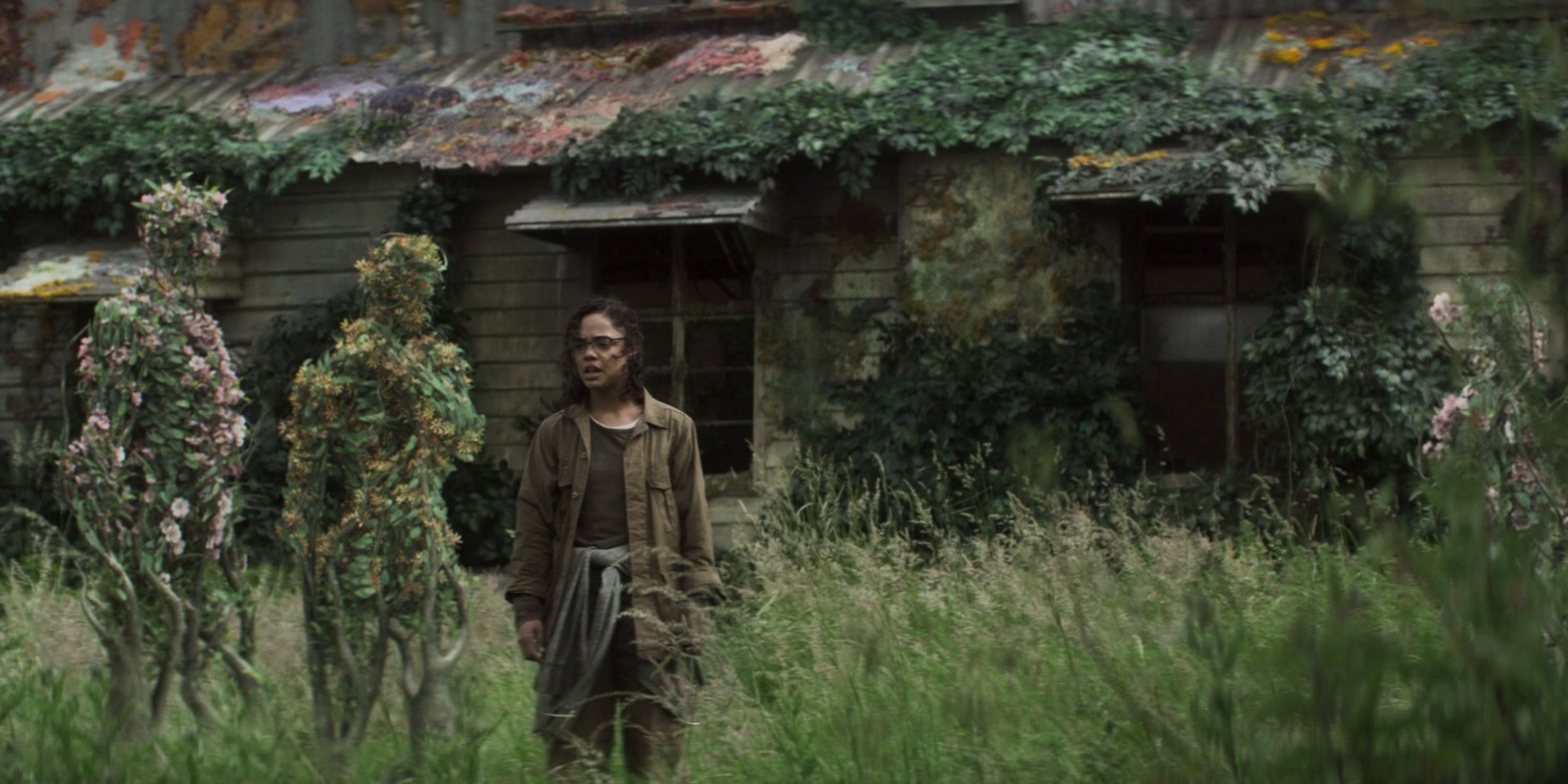 a woman stands in front of a house with plants in the form of people